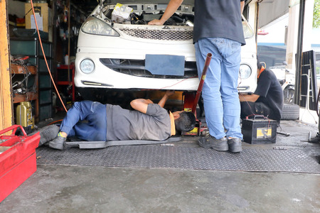 Young male car mechanic checking repairing under vehicleの写真素材