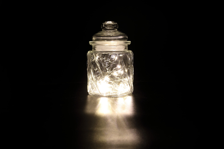 Shining light through glass jar transparent decorated on dark black background の写真素材