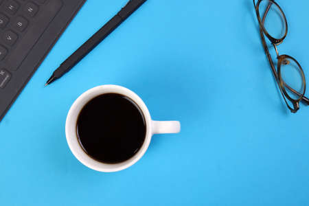 Black computer keyboard eyeglass coffee cup pen on blue white background top view copy text spaceの写真素材