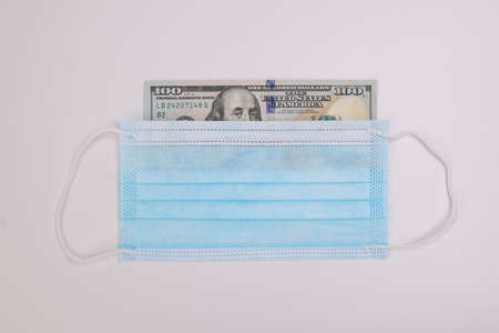 US Dollar currency paper money 100 Hundred dollar bill peaking through surgical anti virus mask on...