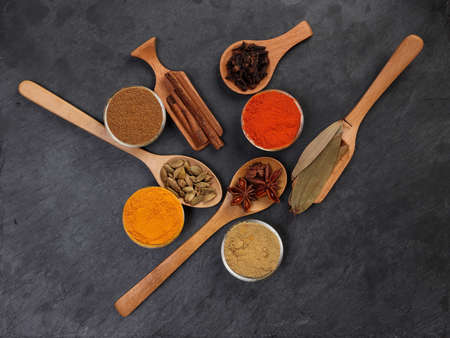 Mix variety spice cinnamon cardamom clove bay leaf wooden chilli cumin turmeric powered on black slate backgroundの写真素材
