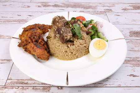 Beef Biryani Tehari with boiled egg coriander leaf garnish chicken curry pot roasted leg tomato cucumber onion chili coriander salad on white plate set over rustic wood backgroundの写真素材