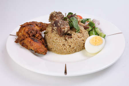 Beef Biryani Tehari with boiled egg coriander leaf garnish chicken curry pot roasted leg tomato cucumber onion chili coriander salad on white plate set over white backgroundの写真素材