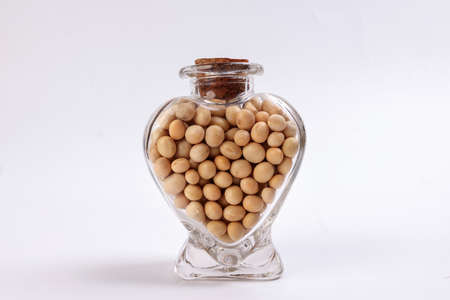 Soya beans in a hart shape glass bottle on white background