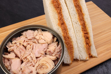 Tuna fish spread sandwich white bread on wooden board over tuna flake chunk in tin can black slate backgroundの写真素材