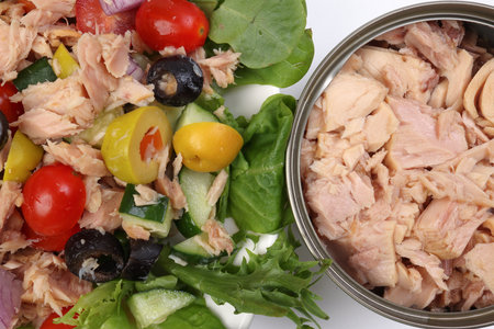 Tuna fish meat salad cucumber tomato onion black green olive leaf lettuce on white plate tuna flake chunk in tin can over white backgroundの写真素材