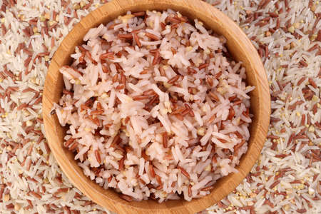 Cooked and raw mixed low glycaemic index healthy rice grain basmati millet buckwheat red rice in wooden bowl over wooden plate on white backgroundの写真素材