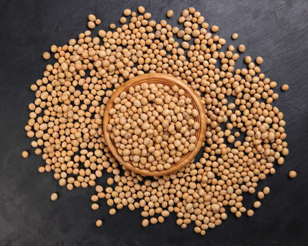Soyabeans soya beans in wooden bowl flowing over black slate stone background copy text space flat lay top viewの写真素材