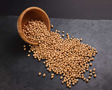 Soyabeans soya beans in wooden bowl flowing over black slate stone background copy text space flat lay top viewの写真素材