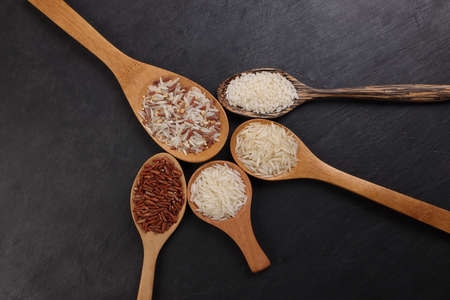 Long grain basmati medium grain jasmine short grain pilaf polau risotto brown low glycaemic index gi rice in wooden spoon on black background copy text space top flat lay viewの写真素材