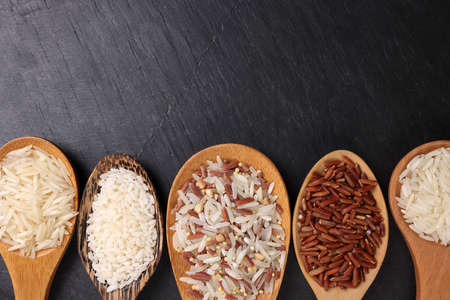 Long grain basmati medium grain jasmine short grain pilaf polau risotto brown low glycaemic index gi rice in wooden spoon on black background copy text space top flat lay viewの写真素材