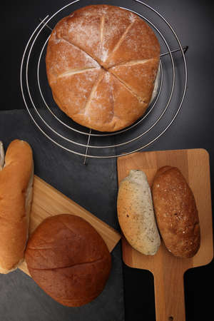 Freshly baked bread loaf bun roll round long mix verity on wooden board metal grill over black...