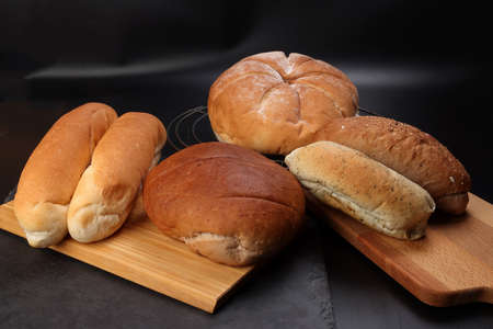 Freshly baked bread loaf bun roll round long mix verity on wooden board metal grill over black...