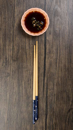 Bamboo wooden chopsticks and chili soya sauce in small ceramic bowl dish on rustic wood backgroundの写真素材