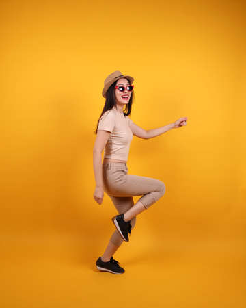Beautiful young south east Asian woman red frame sunglass hat pose act walk move forward on yellow...