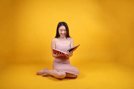 Beautiful young south east Asian woman sit down on floor yellow orange color background read study...