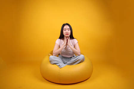 Beautiful young south east Asian woman sits on a yellow beanbag seat orange yellow color background...