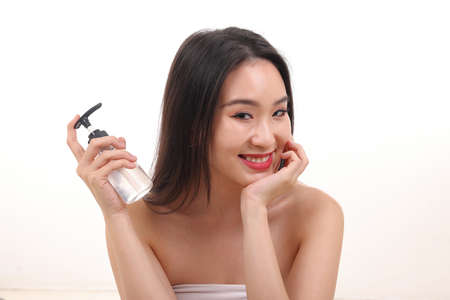 Beautiful young south east Asian woman posing holding using squeeze transparent liquid hand sanitizer plastic bottle pose see offer white backgroundの写真素材