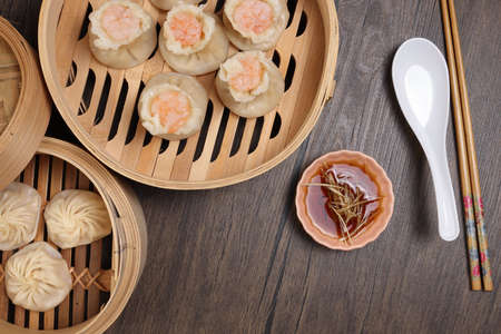 Prawn shrimp shaomai Xiao long bao dim sum dumpling chicken prawn fish seafood vegetable in bamboo steamer sauce chopsticks on rustic background