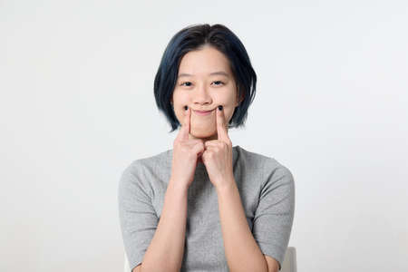 Young attractive Asian chinese malay woman pose face body expression mode emotion on white background smiley face with fingerの写真素材