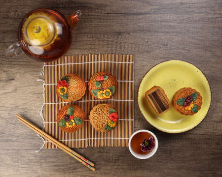 Colourful flower decorated mooncake Chinese mid autumn festival on bamboo food mat background slice cut piece layered on yellow ceramic plate glass teapot teacup chopsticksの写真素材