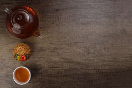 Colourful flower decorated mooncake cut slice half layer Chinese mid autumn festival on glass teapot white ceramic teacup over rustic wood border copy text spaceの写真素材