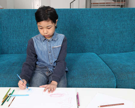 Southeast Asian child girl female special need medical down adhd autism syndrome play draw doodle writing look happy smile emotion expression blue color book smart phone sofaの写真素材