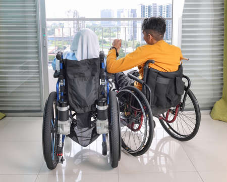 South east Asian malay man woman couple headscarf tudung middle aged disabled on wheelchair looking sitting in front of balcony window look outside holding handの写真素材