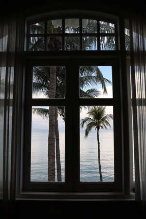 Beautiful view through window palm trees ocean sea blue water cloudy sky