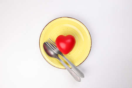 ceramic retro yellow food plate fork spoon with three dimension 3d red hart symbol on top of it white background copy text space top viewの写真素材