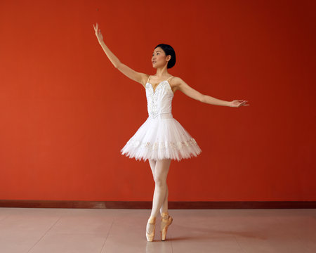 Beautiful Asian woman ballet dancer practice dance jump move wearing tutu at home red orange background wallの写真素材
