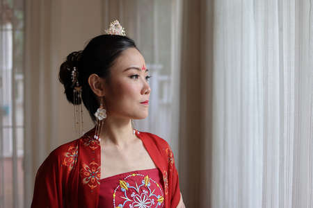 Young attractive Asian woman wearing tadeonal Chinese red hanfu long skirt dress costume scarf hairpin earing indoor natural lightの写真素材