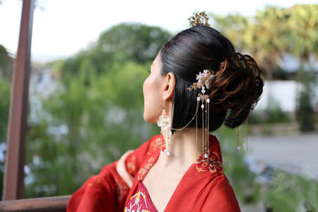 Young attractive Asian woman wearing tadeonal Chinese red hanfu long skirt dress costume scarf hairpin earing decorated outdoor green garden patioの写真素材