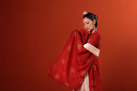 Young attractive Asian woman wearing tadeonal Chinese red hanfu long skirt dress costume scarf hairpin earring indoor on read marron background wallの写真素材