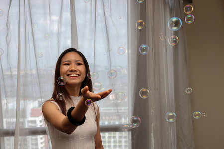 Young Asian woman indoors blowing soap bubble flying happy smile fun