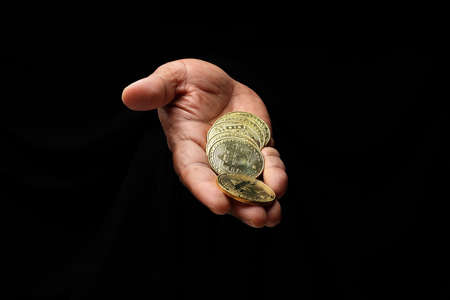 Asian male dark skinned single hand fist finger on black background holding golden fake sample physical bitcoin cryptocurrencyの写真素材