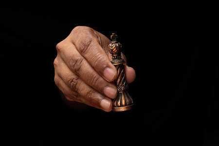 Asian male dark skinned single hand fist finger on black background holding game metal chess king