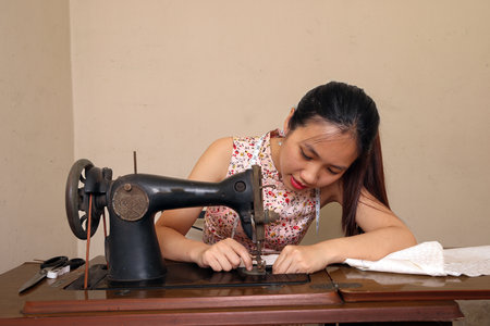 Young Asian woman using tailoring cloth fabric on a retro vintage old sewing machineの写真素材