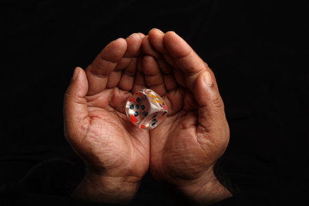 Asian dark skin top view two hand finger holding playing dice gamble luck on black backgroundの写真素材