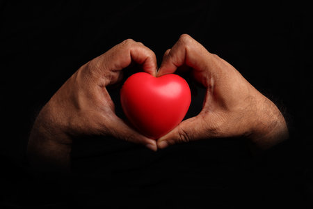 Asian dark skin top view two hand holding making red hart love shape sign on black backgroundの写真素材