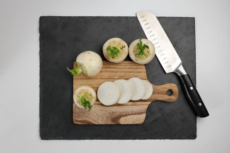 Small white round snowball radish on white background cut sliced diced stacked wooden chopping board...