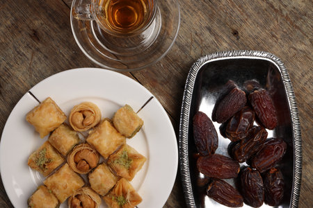 Layered stuffed pastry Baklava middle eastern sweet dessert dry ripe sweet date fruit tea in transparent glass cup saucer on rustic wooden backgroundの写真素材