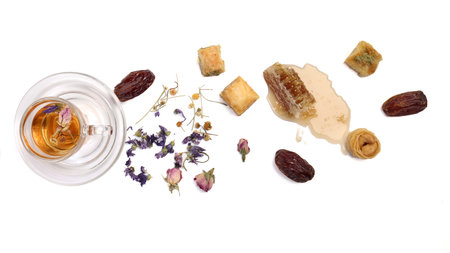 Layered stuffed pastry Baklava sweet dessert  date fruit liquid honey natural geomatic hexagon bee wax honeycomb  flower tea rose bud butterfly pea chamomile flower tea in transparent glass cup saucer on white backgroundの写真素材