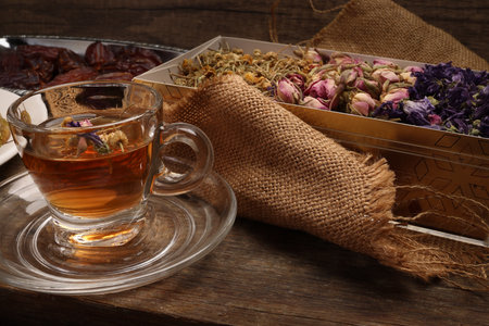 Layered stuffed pastry Baklava middle eastern sweet dessert dry ripe sweet date fruit dry flower tea rose bud butterfly pea chamomile flower tea in transparent glass cup saucer on rustic wooden backgroundの写真素材