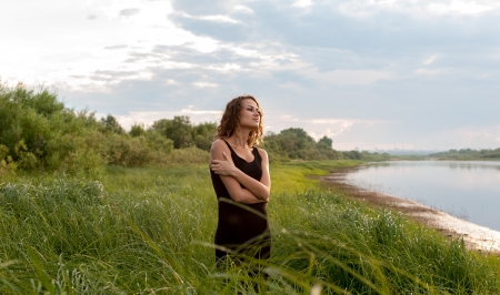 Beautiful girl walks and dreams in high grass on the banks of riverの写真素材