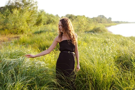 Beautiful girl walks and dreams in high grass on the banks of riverの写真素材