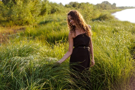 Beautiful girl walks and dreams in high grass on the banks of riverの写真素材