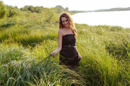 Beautiful girl walks and dreams in high grass on the banks of riverの写真素材