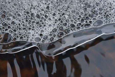 The accumulation of air bubbles under the thin crust of ice against the background of a turbulent flow of water.の写真素材