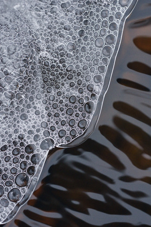 The accumulation of air bubbles under the thin crust of ice against the background of a turbulent flow of water.の写真素材